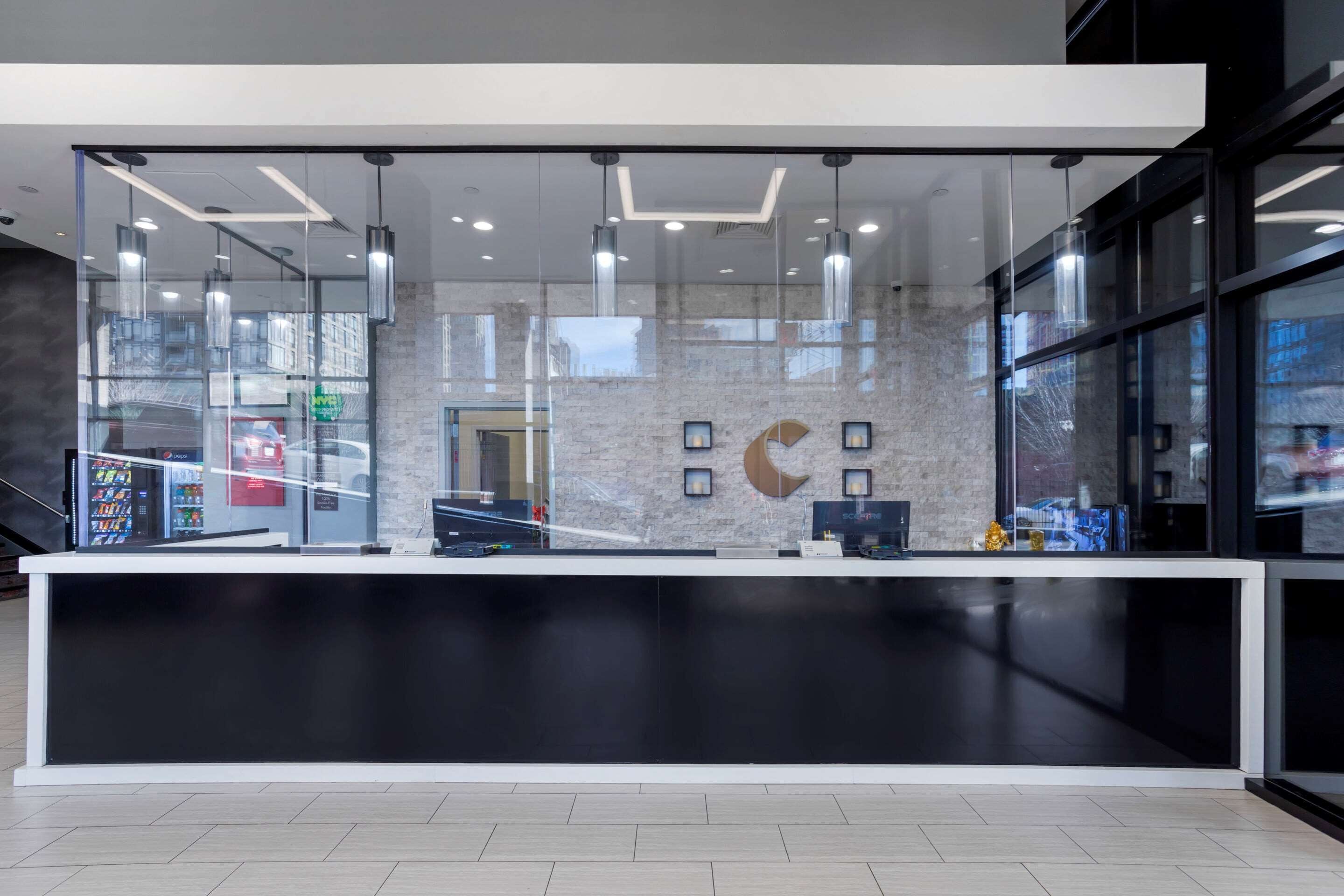 A modern reception desk with a glass partition, a computer, and a cash register.