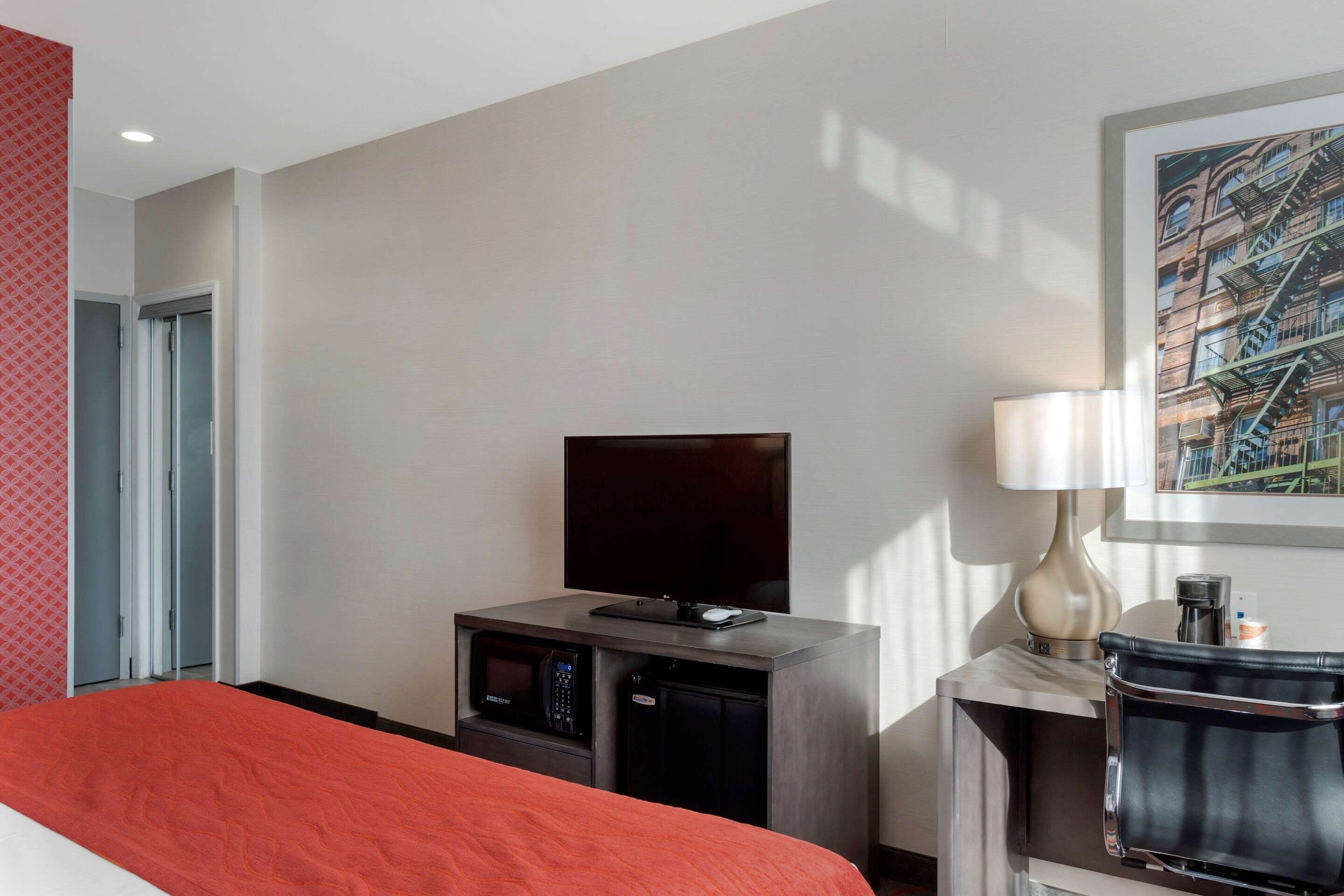 A hotel room with a bed, a TV, a desk with a lamp, a coffee machine, and a microwave.