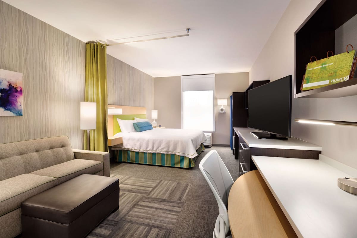 A hotel room with a sofa, bed, desk, TV, and a painting on the wall.