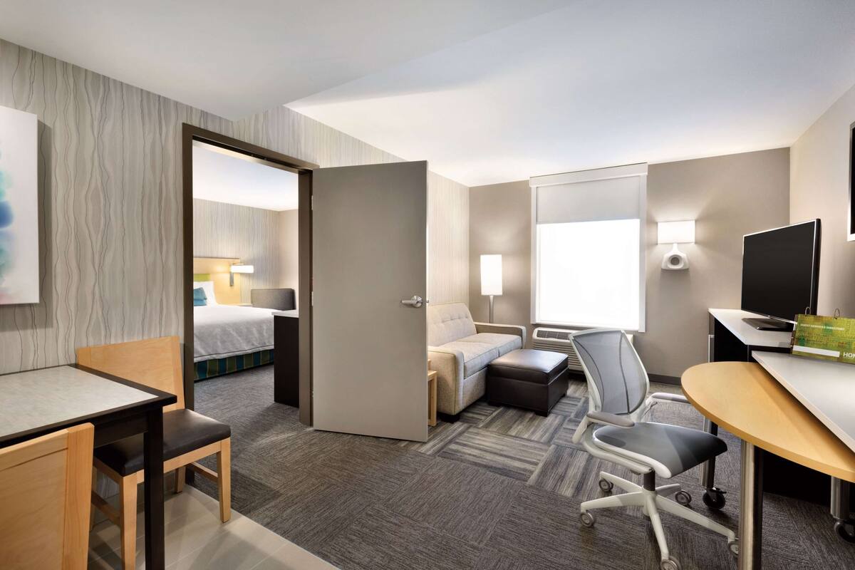 A hotel room with a bed, a desk, a chair, a sofa, and a TV.