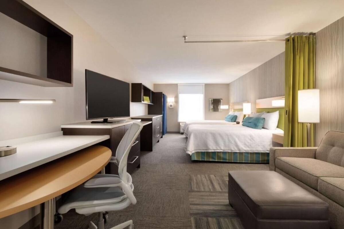A hotel room with a desk, chair, bed, and a sofa.