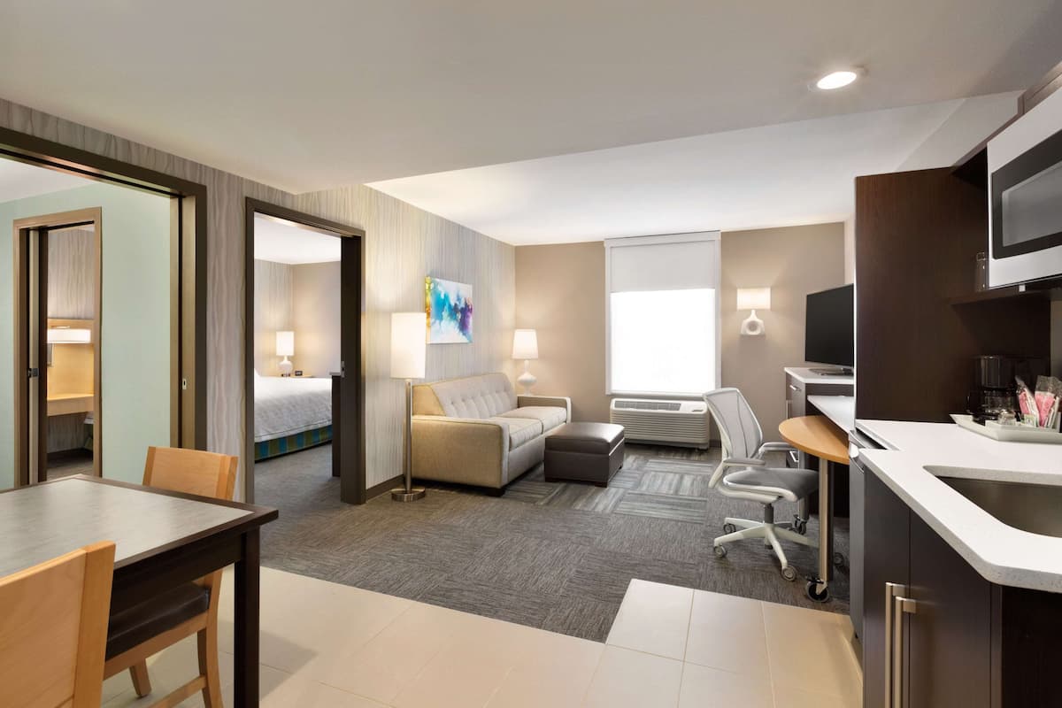 A hotel room with a bed, a sofa, a desk, and a kitchenette.