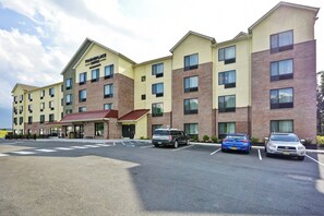 Een hotel met een centrale ingang, meerdere verdiepingen en een parkeerplaats met verschillende auto's.