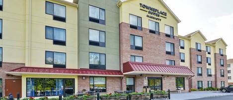 A multi-story hotel with a yellow facade, a red awning, and a sign that reads "Towneplace Suites."