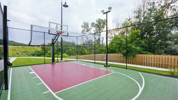 Uma quadra de basquete ao ar livre com superfície verde e vermelha, cercada por uma grade e árvores.