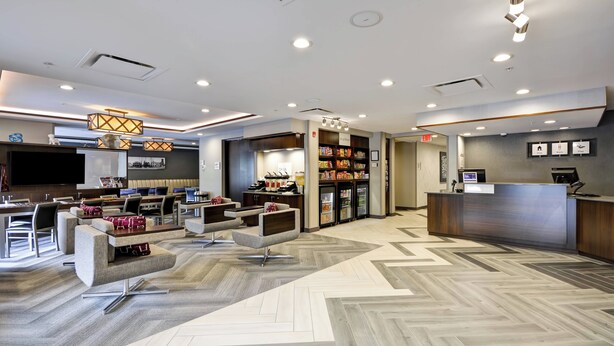 A modern hotel lobby with seating areas, a reception desk, and a food display. - Towneplace Suites Dover Rockaway (Dover)