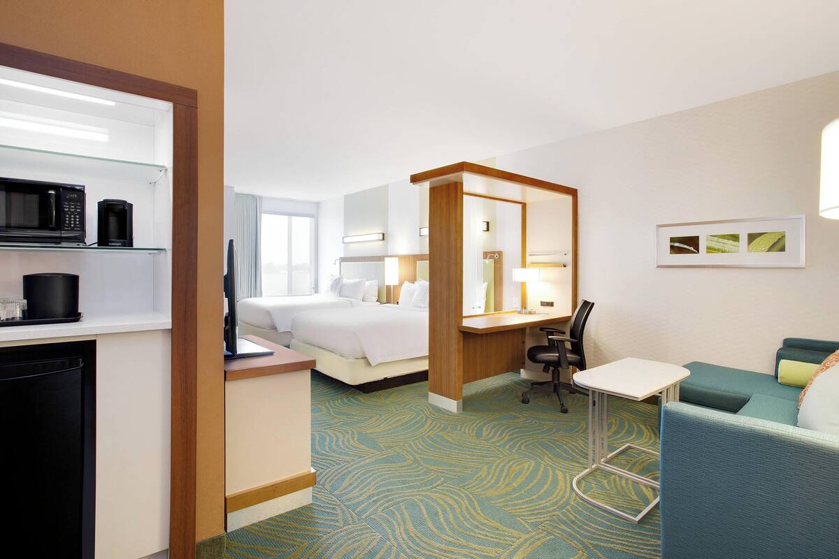 A hotel room with a bed, a desk with a chair, a microwave, a coffee maker, and a small table.