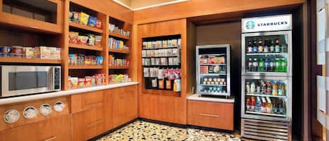 A kitchenette with a microwave, shelves stocked with snacks, a refrigerator, and a Starbucks vending machine.