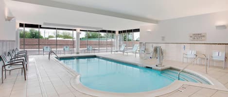 An indoor swimming pool with clear glass walls, a tiled floor, and a warning sign on the wall.