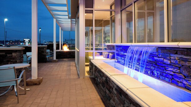 Un patio con mobiliario exterior, pared de piedra y una cascada.