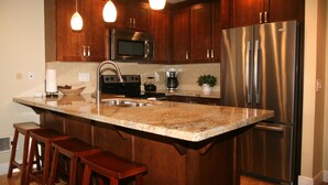 A kitchen with wooden cabinets, stainless steel appliances, a granite countertop, and pendant lighting. - Luxury on the Beach (Oceanside)