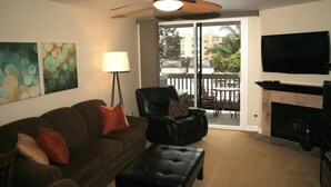 A living room with a sofa, a black leather chair, a black ottoman, a ceiling fan, a flat-screen TV, and a fireplace. - Luxury on the Beach (Oceanside)