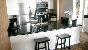 Eine moderne Küche mit weißen Schränken, Edelstahlgeräten, einer schwarzen Granitabdeckung und zwei schwarzen Barhocker.