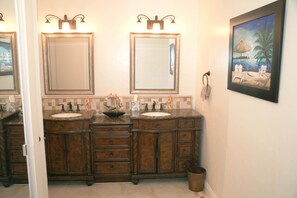 A bathroom with two sinks, a large mirror, and a painting of a beach scene. - Panoramic Perfection (Oceanside)