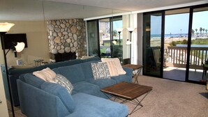 A living room with a blue sofa, a wooden coffee table, and a stone wall. - Harbor Cottage (Oceanside)