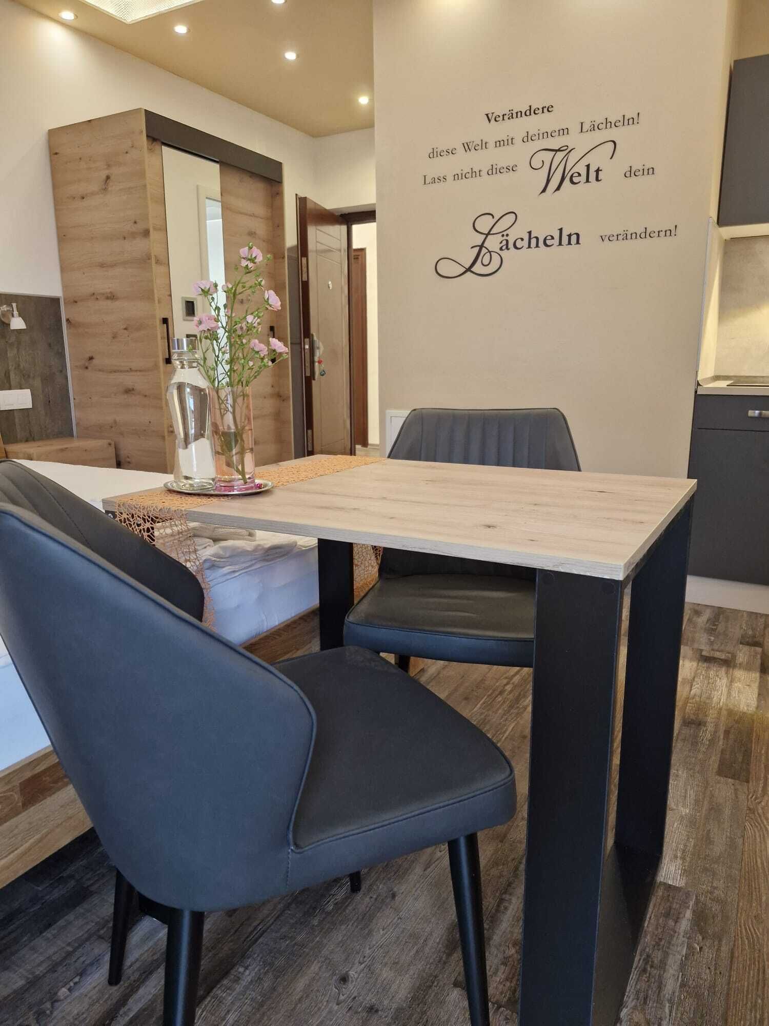 A modern dining area with a wooden table, black chairs, and a decorative wall with a motivational quote.