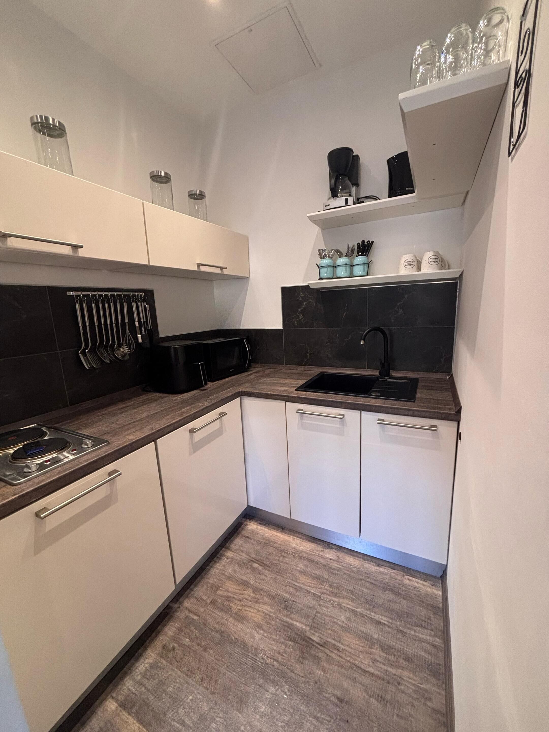 A modern kitchen with white cabinets, a black countertop, and a black backsplash. There is a sink, a stove, and a coffee maker on the countertop.