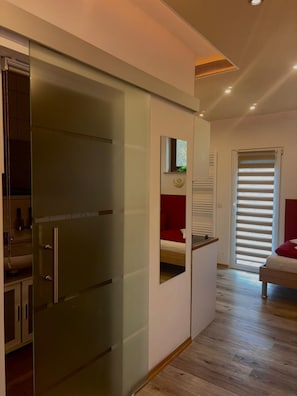 Une chambre à coucher moderne avec un placard à portes coulissantes en verre, un lit avec une literie rouge et un petit espace bureau.