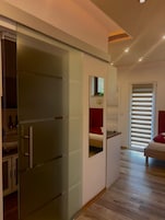 Un dormitorio moderno con armario de puertas correderas de vidrio, cama con ropa de cama roja y un pequeño escritorio.