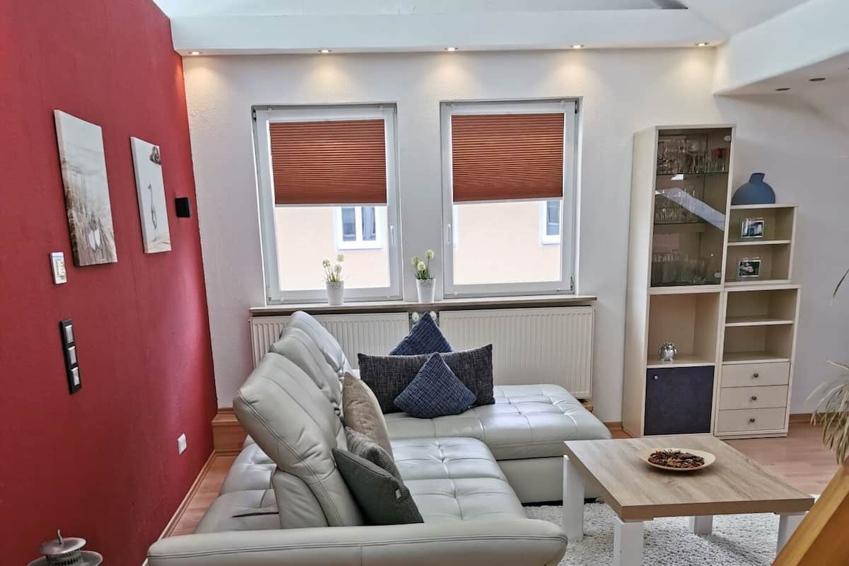 Ein modernes Wohnzimmer mit einer Eckcouch, einem Holztisch und einer roten Akzentwand.