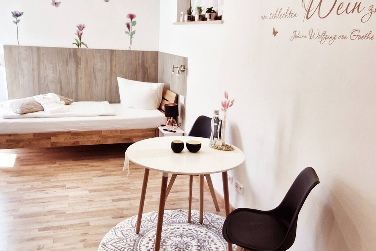 Ein modernes Schlafzimmer mit einem Holzkopfteil, einem runden Esstisch mit zwei Stühlen und einer Wand mit einer dekorativen Schrift.