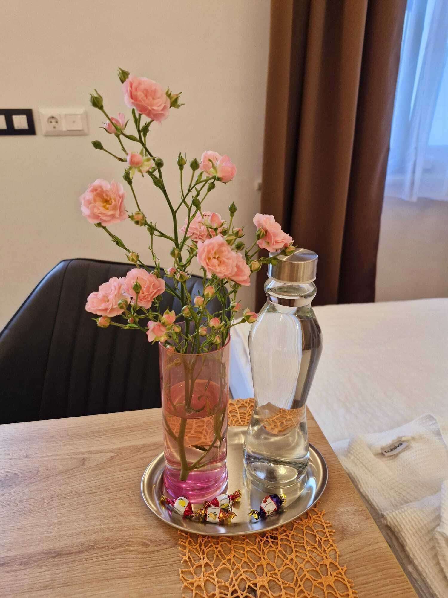 Uma mesa com um vaso de flores cor-de-rosa, um saleiro e alguns doces embalados.