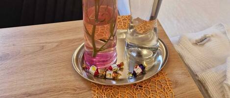 Uma mesa com um vaso de flores cor-de-rosa, um saleiro e alguns doces embalados.