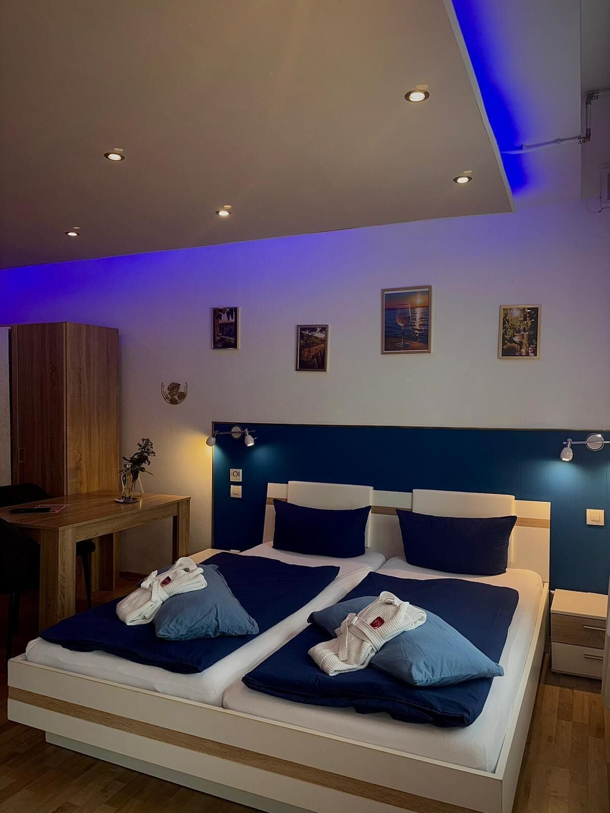 A double bed with a headboard, bedside tables, a desk, and wall-mounted artwork.