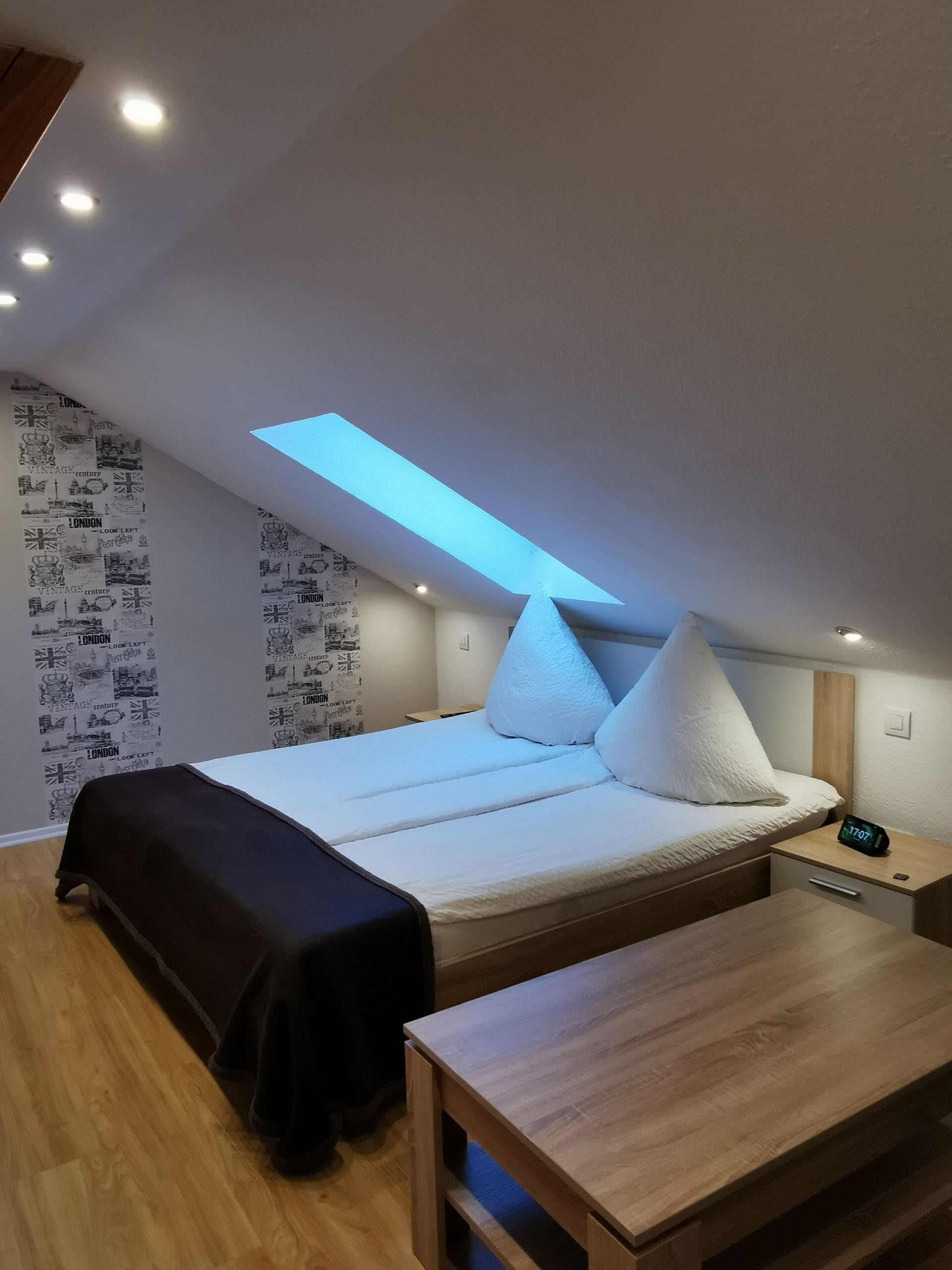 A modern bedroom with a skylight, a bed with white bedding, a bedside table, and a wooden bench.