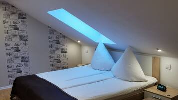 A modern bedroom with a skylight, a bed with white bedding, a bedside table, and a wooden bench.
