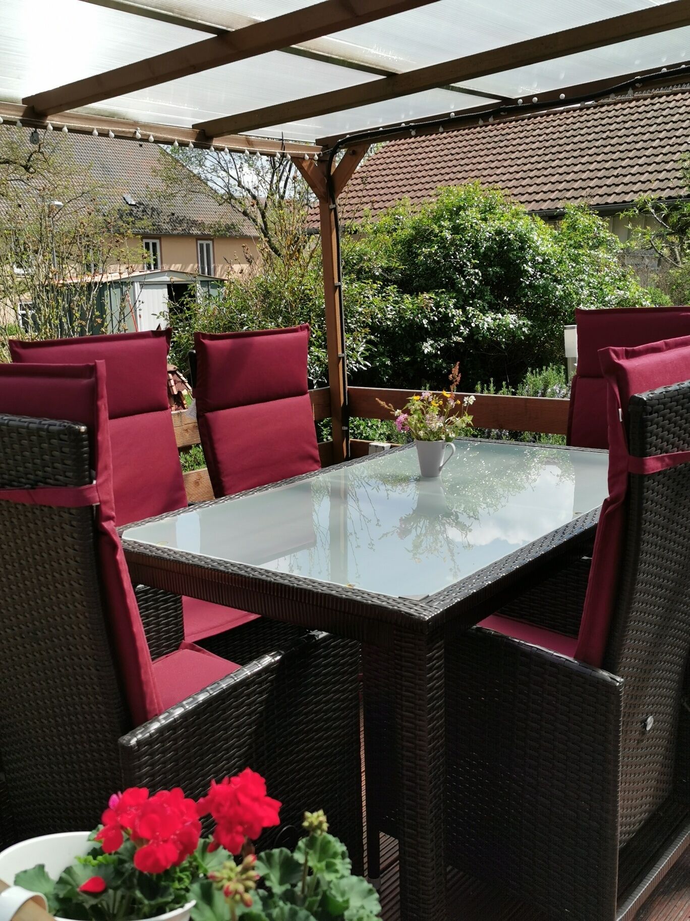 An outdoor patio with a glass-top table and wicker chairs with red cushions.