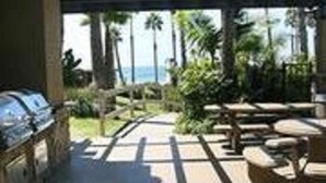 An outdoor patio area with a grill, seating, and a view of the ocean. - Steps to the Sand (Oceanside)