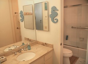 Un baño con lavamanos, dos espejos, un adorno con forma de caballito de mar y zona de ducha.
