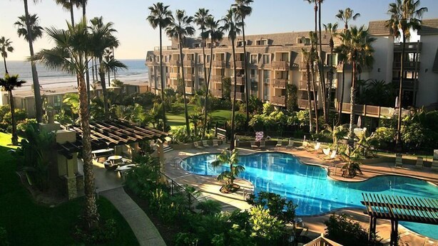 A hotel with a pool, palm trees, and a view of the ocean. - Steps to the Sand (Oceanside)