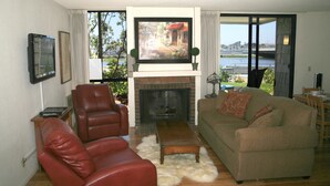 A living room with a fireplace, leather chairs, a sofa, and a television mounted above it. - Steps to the Sand (Oceanside)
