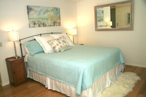 Un dormitorio con cama, dos lámparas de noche, una mesita de noche, una alfombra mullida, un cuadro y un espejo en la pared.