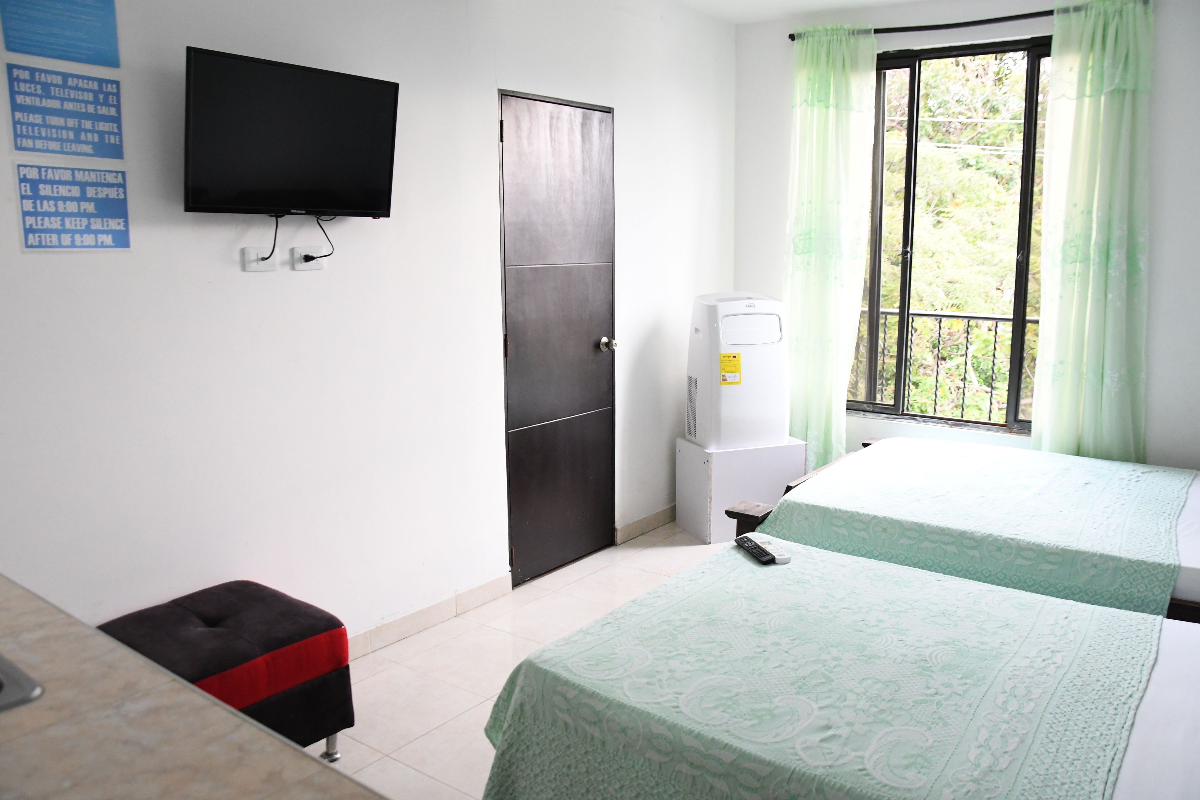 Habitación de hotel con cama, televisión en la pared, dispensador de agua y ventana con cortinas.