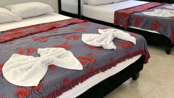Habitación de hotel con dos camas, cada una con una colcha estampada en rojo y azul y toallas blancas. Hay un espejo grande en una pared, y el piso está cubierto de baldosas.