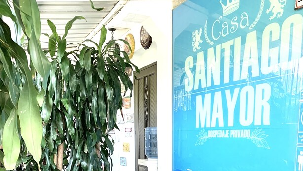A room with a black leather sofa, a small table with a laptop, and a large poster reading "Casa Santiago Mayor." - Casa Santiago Mayor (Cali)