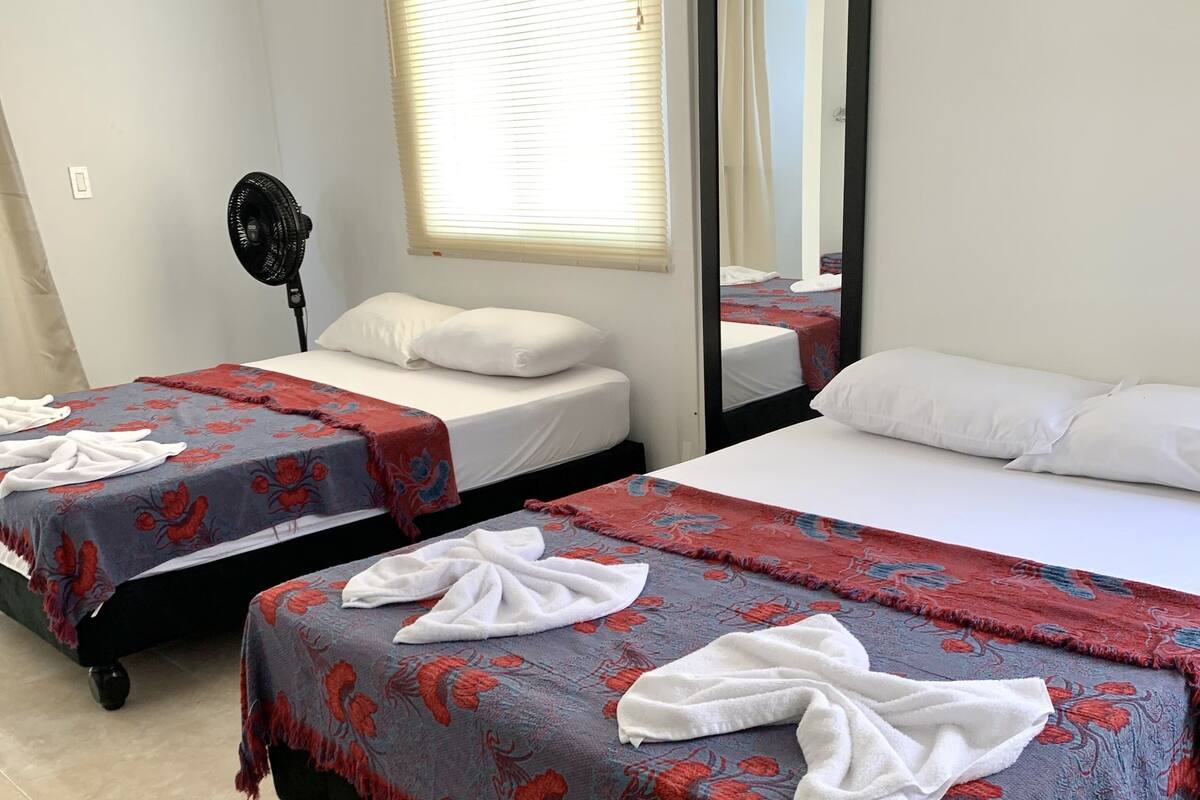 Hotellihuoneessa on kaksi sänkyä, joissa on kummassakin kukkakuviollinen päiväpeite ja valkoiset tyynyt. Huoneessa on myös lattiatuuletin ja ikkuna, jossa on sälekaihtimet.