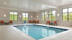 A large indoor swimming pool with clear blue water, surrounded by orange chairs and tables, and large windows providing natural light. - Hampton Inn North Olmsted Cleveland Airport (North Olmsted)