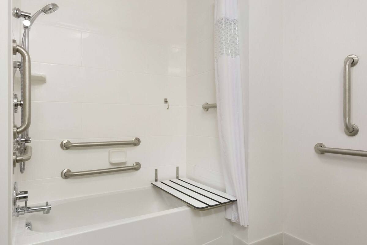 Une salle de bain moderne avec une douche à l’italienne, des barres d’appui et un mur recouvert de carreaux blancs.