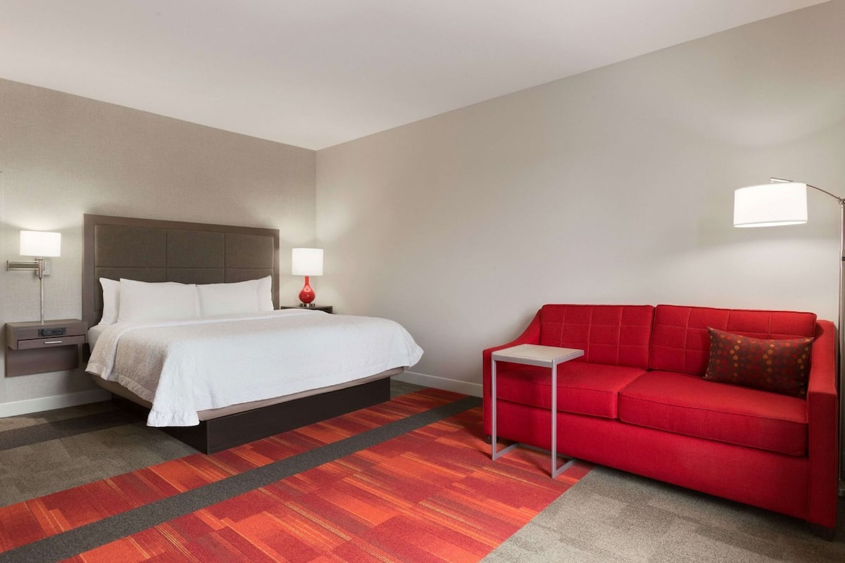 A hotel room with a bed, bedside tables, a red sofa, and a small side table.