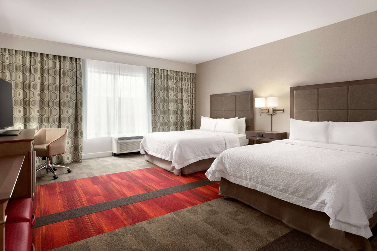 Une chambre d’hôtel avec deux lits, un bureau, une chaise et un téléviseur.
