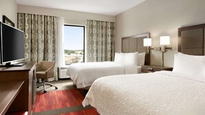 A hotel room with two beds, a desk with a TV, a chair, and a view of the city. - Hampton Inn North Olmsted Cleveland Airport (North Olmsted)