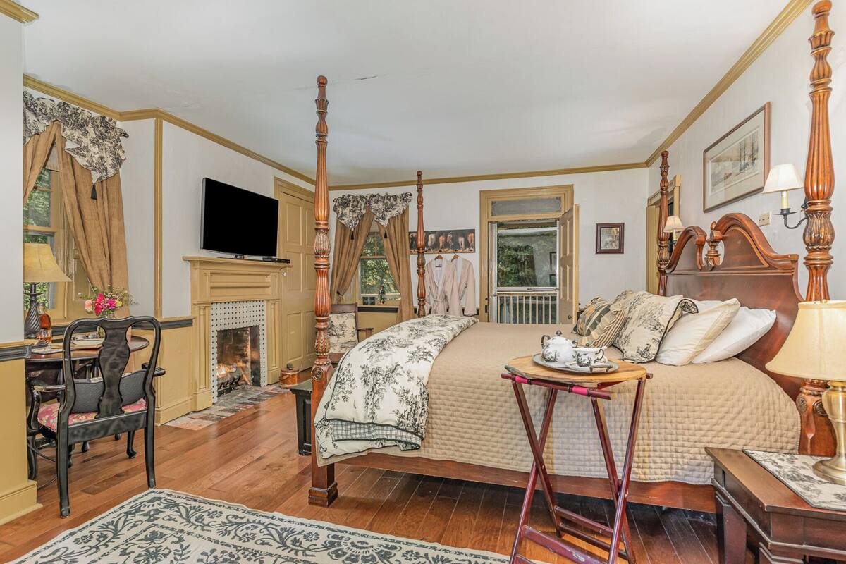 Una cama con dosel, un televisor encima, una chimenea y un rincón comedor con una silla y una mesa.