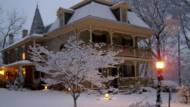 Une grande maison à deux étages, dont le toit est recouvert de neige et qui possède un balcon.