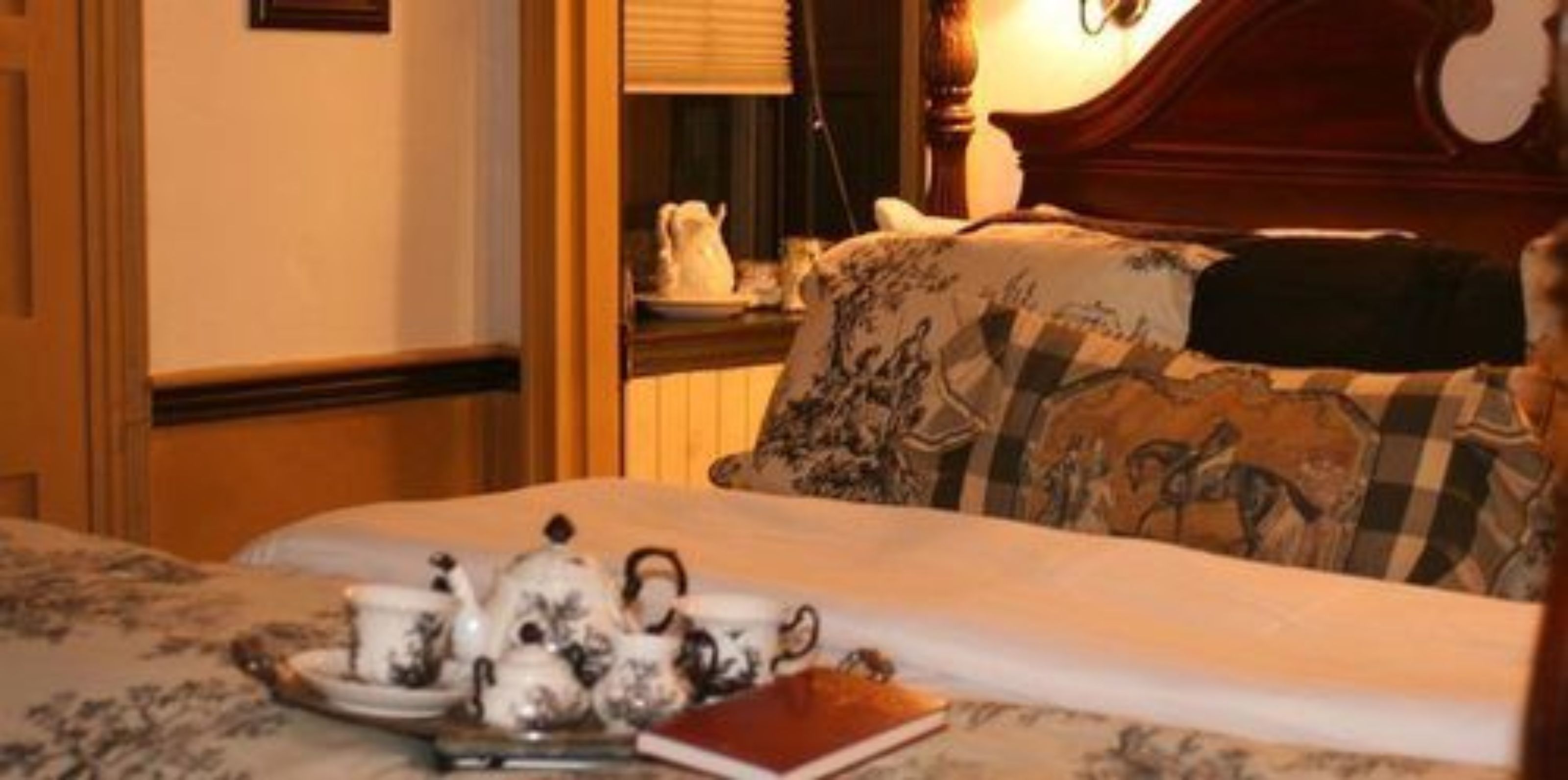 A hotel room with a neatly made bed, a bedside table with a teapot and cups, and a book.