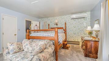 A bedroom with a wooden four-poster bed, a floral sofa, a wooden dresser, and a nightstand with a lamp.