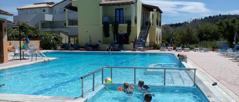 A swimming pool with a children's play area, lounge chairs, and a building with a satellite dish.